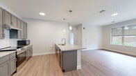 This well-appointed 3-bedroom, 2-bathroom unit in Rochester, MN offers a thoughtfully designed single-floor layout with modern finishes throughout. The open-concept kitchen serves as the heart of the home, featuring gray shaker-style cabinetry, granite countertops, a center island with a built-in sink, subway tile backsplash, stainless steel appliances including a refrigerator and range, and pendant lighting — all flowing seamlessly into the living area. Light wood-tone vinyl flooring runs throughout, creating a cohesive and easy-to-maintain aesthetic. The three bedrooms are generously sized, filled with natural light from large windows, and include access to walk-in closets with wire shelving systems. The primary bedroom offers its own dedicated bathroom with a granite-topped vanity, gray cabinetry, and a walk-in shower. The second bathroom mirrors the same quality finishes with a full shower/tub combination and matching vanity. Additional conveniences include in-unit laundry, a utility room, and ample closet storage with four closets total. Neutral wall tones and clean architectural lines give the space a bright, contemporary ambiance suited for comfortable everyday living.