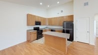 This single-floor residence offers a thoughtfully designed layout that balances functionality and comfort throughout. The kitchen serves as a central highlight, featuring warm honey-toned cabinetry extending to the ceiling for ample storage, granite-look countertops, a full suite of black appliances including a range, microwave, dishwasher, and refrigerator, and a central island providing additional prep and seating space. Light hardwood flooring runs through the main living and kitchen areas, adding warmth and continuity to the open layout. The living area is generously sized, bathed in natural light, and finished with a ceiling fan overhead. The bedrooms are carpeted for comfort and each benefit from ceiling fans and multiple windows that invite natural light. The primary bedroom includes access to a spacious walk-in closet outfitted with wire shelving and hanging rods, offering excellent storage capacity. Two full bathrooms mirror each other in design, each featuring a tub-shower combination with tiled surrounds, a vanity with wood cabinetry and a white countertop, an illuminated mirror, and neutral tile flooring. Clean white walls throughout the residence create a bright, move-in-ready atmosphere well-suited for a variety of living styles.