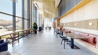 Located at 39 Bruton Street in San Francisco, CA, this expansive single-floor commercial space offers an impressive blend of industrial architecture and refined design. The grand lobby sets the tone immediately, featuring polished terrazzo flooring, raw exposed concrete walls, and soaring double-height ceilings that amplify the sense of openness. Floor-to-ceiling curtain glass walls flood the interior with abundant natural light while framing sweeping outdoor views of the surrounding cityscape.

Curated art installations are woven throughout the space, including a striking sculptural wall piece composed of organic ceramic and metallic forms, alongside a live-edge natural wood reception desk resting on brass supports. A shimmering mosaic tile feature wall anchors another area, complemented by lush potted greenery and sculptural seating.

The lounge area provides a welcoming environment with a mix of mid-century and contemporary furnishings arranged beneath a dramatic pendant chandelier. Corridors feature iridescent fluted tile cladding that casts prismatic reflections, adding a bold visual contrast to the muted concrete and dark wood paneling found elsewhere. A staircase with glass railings connects levels within the space.

Private office areas are thoughtfully appointed with marble-topped desks and curated artwork. Throughout, the design strikes a balance between raw materiality and elevated sophistication, creating a dynamic and inspiring environment.