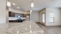 This well-appointed single-story home offers three bedrooms, two bathrooms, and a thoughtfully designed layout that maximizes functionality and comfort. The open-concept kitchen and living area serves as the heart of the home, showcasing a large granite-topped island with an undermount sink and stylish pendant lighting. Dark cabinetry, a subway tile backsplash, and a full suite of stainless steel appliances complete the kitchen. The adjacent living room features wood-look flooring, a ceiling fan, and multiple windows that invite natural light throughout. The bedrooms vary in character — the primary bedroom includes wood-look flooring, a ceiling fan, and access to a dedicated en-suite bathroom and walk-in closet with built-in shelving. Secondary bedrooms feature plush carpeting, ceiling fans, and generous natural light from large windows. Each bedroom also includes its own closet. The primary en-suite bathroom is equipped with a glass-enclosed walk-in shower, while the second bathroom offers a soaking tub with marble-style tile surround, granite countertops, and dark cabinetry. A hallway connects the bedrooms and three closets, providing ample storage throughout. The neutral color palette and modern finishes create a clean, cohesive aesthetic across the entire home.