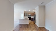 Located in Greensboro, NC, this single-floor residence offers a well-designed open-concept layout with thoughtful finishes throughout. The kitchen serves as the heart of the home, showcasing granite countertop surfaces, a central island with an undermount sink, rich two-tone cabinetry with frosted glass upper doors, a classic subway tile backsplash, and a full suite of stainless steel appliances. Hardwood-style flooring flows seamlessly through the kitchen and main living areas, transitioning to plush carpeting in the bedrooms. Crown molding adds an elegant architectural detail to the main living spaces. The bedrooms are generously proportioned, each featuring large windows with blinds that invite ample natural light and outdoor views. One bedroom provides direct access to a private balcony through glass French doors, complemented by a ceiling fan overhead. Walk-in closets with wire shelving systems offer organized storage. The bathrooms are finished with granite-topped white shaker vanities, modern fixtures, and hardwood-style flooring. Additional storage cabinetry is featured in one of the bathrooms. Recessed lighting throughout the home ensures a bright, welcoming ambiance across all areas of this clean, contemporary residence.