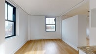 This well-appointed single-floor urban unit showcases a clean, contemporary design throughout. Light-toned hardwood flooring runs consistently across all rooms, creating a warm and cohesive aesthetic that contrasts beautifully with the crisp white walls and ceilings.

The kitchen is efficiently designed with tall white cabinetry featuring black hardware, granite countertops, a stainless steel sink, and a full suite of stainless steel appliances including an electric range and over-the-range microwave. White subway tile backsplash adds a classic touch, while the space is accessed through a bold dark gray entry door with smart lock technology.

Multiple rooms provide flexible living and sleeping arrangements, each featuring the same warm hardwood flooring and bright white walls. Black-framed windows throughout admit generous natural light and offer views of the surrounding urban landscape, including glimpses of neighboring brick buildings and city skyline elements.

The bathroom is finished to a high standard, featuring white subway tile walls, large-format gray floor tiles, a wall-mounted dark wood vanity with an integrated white basin, a recessed mirror with wall-mounted lighting, and a full bathtub with a glass sliding shower enclosure. The overall ambiance of the unit is modern, minimal, and move-in ready.