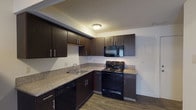 This two-floor residence offers a well-organized layout designed for comfortable everyday living. The kitchen is a standout feature, equipped with dark espresso-toned cabinetry, granite-style countertops, and a full suite of black appliances including a range, over-the-range microwave, dishwasher, and refrigerator. The L-shaped counter configuration maximizes workspace, while wood-style plank flooring ties the kitchen seamlessly into the adjacent living area. The main living space is open and versatile, benefiting from a neutral color palette and durable wood-style flooring that extends throughout the lower level. A carpeted staircase connects the two floors, leading to the upper level where plush carpet continues into a generously sized bedroom. The bedroom features a window for natural light and direct access to a spacious walk-in closet outfitted with wire shelving and hanging rods on multiple walls. The full bathroom includes a tub/shower combination, a vanity with granite-style countertop, dark cabinetry, and wood-style flooring. Textured ceilings are present throughout, and the clean white walls create a bright, neutral backdrop across both levels of the home.