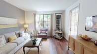 This single-floor residence offers a cohesive and carefully designed layout that balances comfort with style. The living room serves as the heart of the home, featuring rich hardwood flooring, large multi-pane windows that frame lush greenery outside, and a neutral color palette accented by a warm gray feature wall. Natural light flows generously through the space, highlighting the open and airy atmosphere.

The dining area transitions seamlessly from the living room, offering ample space for entertaining with vaulted ceiling details and access to adjoining rooms. The galley-style kitchen is outfitted with white shaker cabinetry, dark countertops, black appliances, a gas range, and a dedicated walk-in pantry for generous storage.

Two bedrooms provide restful retreats, each carpeted for warmth and comfort, with large windows overlooking greenery and closet space for storage. The bathroom features classic white subway tile surrounding a full soaking tub and shower, complemented by hardwood-style flooring and clean, minimal finishes.

Throughout the residence, consistent hardwood flooring, crisp white walls, and thoughtful architectural details create a unified, welcoming ambiance suitable for both everyday living and entertaining.