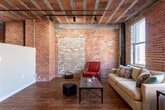 Located at 200 Walnut St in Kansas City, MO, this single-floor urban loft beautifully blends historic industrial character with modern conveniences. The space is defined by its striking exposed brick walls, raw concrete columns, and open-beam ceilings with visible ductwork and track lighting — hallmarks of classic loft-style architecture that give the space an authentic, industrial aesthetic.

Rich hardwood floors run throughout the main living areas, anchoring the open-concept layout that connects the kitchen and living room seamlessly. The living area is bright and airy, with large windows that draw in natural light and offer views of the surrounding neighborhood. The kitchen is well-appointed with light maple cabinetry, dark granite countertops, stainless steel appliances including a refrigerator, range, and built-in microwave, and a breakfast bar with seating — ideal for casual dining and entertaining.

The bathroom features a clean, functional design with a granite-topped vanity, maple cabinetry, and a full shower-tub combination. A dedicated laundry area houses a full-size washer and dryer with overhead storage cabinetry, adding everyday practicality to this characterful space. Throughout, the interplay of raw historic materials and updated finishes creates a warm, inviting atmosphere unique to Kansas City's vibrant downtown core.