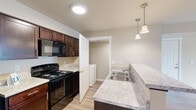Located at 11103 W Sixth Ave in Airway Heights, Washington, Unit B203 is a thoughtfully designed single-floor residence that balances comfort and functionality. Light-toned luxury vinyl plank flooring flows throughout the main living areas, complemented by warm neutral walls and clean white trim, creating a bright and cohesive aesthetic.

The kitchen is a standout feature, equipped with rich dark-wood cabinetry, light granite-style countertops, and a full suite of black appliances including a refrigerator, electric range with overhead microwave, and a double-basin stainless steel sink. Elegant pendant lighting above the counter adds a refined touch, while recessed ceiling lights provide ample illumination. A convenient in-unit washer is tucked just off the kitchen, adding everyday practicality.

The living area is open and airy, with a large window dressed in horizontal blinds that invite natural light and a glass-panel door providing direct access to an outdoor balcony. A wall-mounted HVAC unit ensures year-round comfort.

The bedroom features plush carpeting for a cozy feel, bathed in soft natural light. The bathroom is finished with matching dark cabinetry, granite-style countertops, a well-lit vanity mirror, and light hardwood-style flooring, offering a clean and functional space. This unit combines modern design elements with practical amenities throughout.