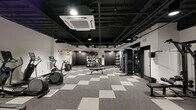 Located at 1901 E York St. in Philadelphia's Fishtown neighborhood, this fitness center offers a well-appointed, single-floor exercise facility designed to support a wide range of training needs. The main exercise room is generously sized, featuring a striking industrial aesthetic with an exposed black ceiling, track lighting, and a bold checkered rubber flooring pattern in gray and white tones that adds both visual interest and functional durability.

The cardio zone is equipped with treadmills, elliptical trainers, and a stationary cycling bike with an interactive display screen. The strength training area includes a multi-station cable machine, dedicated weight benches, and a leg extension machine. A well-stocked functional training corner houses a full rack of kettlebells, medicine balls, stability balls, TRX suspension straps, resistance bands, and a plyo box, catering to dynamic and high-intensity workouts. Wall-mounted mirrors in the strength zone enhance spatial awareness during training.

A separate, smaller room with dark-painted walls and matching rubber flooring provides a private, flexible space suitable for stretching, meditation, or individualized training sessions. The facility is climate-controlled with ceiling-mounted HVAC units, and recessed and track lighting throughout ensures a well-lit, focused training environment.