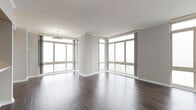 Situated within the prominent City Place building in White Plains, New York, this residence offers a refined and contemporary living environment defined by clean lines, neutral tones, and an abundance of natural light. Dark hardwood flooring flows consistently throughout the main living areas and bedrooms, providing a rich contrast against the soft gray walls and crisp white trim and crown molding detailing.

The main living area is especially notable for its expansive corner window configuration, where floor-to-ceiling glass panels on multiple walls invite sweeping elevated views of the surrounding cityscape and fill the space with generous daylight. Additional rooms continue this window-forward design, each featuring large sliding or casement windows that frame outdoor views and reinforce the airy, open character of the unit.

The kitchen is equipped with stainless steel appliances, including an electric range and over-the-range microwave, complemented by light cabinetry and tile flooring. The bathroom is finished with warm travertine-toned tile on the floors and tub surround, a pedestal sink, oval mirror, and a soaking tub with shower, conveying a clean, timeless aesthetic throughout.