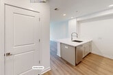 This well-appointed 2-bedroom, 1-bathroom residence offers a thoughtfully designed single-level layout with a clean, modern aesthetic throughout. Light wood flooring flows seamlessly across every room, complemented by crisp white walls and recessed lighting that create a bright, airy atmosphere.

The kitchen is a standout feature, showcasing gray shaker-style cabinetry, quartz countertops, and a full suite of stainless steel appliances including a gas range, microwave, French door refrigerator with ice maker, and a built-in wine cooler. A large island with an undermount sink and a sleek pull-down faucet adds both functionality and style, while a decorative lattice detail above the refrigerator provides a charming architectural accent.

Both bedrooms are comfortably sized with large windows that invite natural light and offer views of the surrounding buildings and landscape. The primary bedroom benefits from a spacious walk-in closet equipped with built-in shelving and dual hanging rods for generous storage. The full bathroom features a soaking tub with a tiled surround in neutral tones and brushed gold fixtures, lending a refined touch to the space.

The overall ambiance is modern, clean, and move-in ready, making it a functional and stylish place to call home.