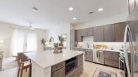This thoughtfully designed single-story residence offers two bedrooms and three bathrooms within a bright, open floor plan. The kitchen serves as the heart of the home, featuring taupe shaker-style cabinetry, stainless steel appliances including a gas range and French door refrigerator, a sleek range hood, and a generously sized island with a quartz countertop and built-in seating — ideal for casual dining and entertaining. Light wood-style flooring flows throughout the main living areas, enhancing the airy, modern aesthetic.

The living room is filled with natural light from a sliding glass door that opens to the outdoors, and is complemented by a ceiling fan overhead. The primary bedroom offers a comfortable retreat with large windows, plush carpeting, and direct access to a spacious en-suite bathroom. The primary bath features a dual-sink vanity with dark wood cabinetry, white quartz counters, built-in shelving, and a walk-in closet. The second bedroom is equally well-lit with large windows and soft carpeting. Each bathroom maintains a clean, contemporary design consistent with the rest of the home. A dedicated laundry room with a stacked washer and dryer adds everyday convenience, rounding out this well-equipped, move-in-ready residence.