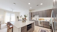 This thoughtfully designed single-story residence offers two bedrooms and three bathrooms within a bright, open floor plan. The kitchen serves as the heart of the home, featuring taupe shaker-style cabinetry, stainless steel appliances including a gas range and French door refrigerator, a sleek range hood, and a generously sized island with a quartz countertop and built-in seating — ideal for casual dining and entertaining. Light wood-style flooring flows throughout the main living areas, enhancing the airy, modern aesthetic.

The living room is filled with natural light from a sliding glass door that opens to the outdoors, and is complemented by a ceiling fan overhead. The primary bedroom offers a comfortable retreat with large windows, plush carpeting, and direct access to a spacious en-suite bathroom. The primary bath features a dual-sink vanity with dark wood cabinetry, white quartz counters, built-in shelving, and a walk-in closet. The second bedroom is equally well-lit with large windows and soft carpeting. Each bathroom maintains a clean, contemporary design consistent with the rest of the home. A dedicated laundry room with a stacked washer and dryer adds everyday convenience, rounding out this well-equipped, move-in-ready residence.