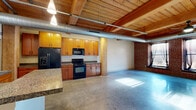 This 2-bedroom, 2-bathroom loft showcases a striking industrial aesthetic, combining raw architectural elements with functional living spaces across a single floor. Exposed wood beam ceilings, polished concrete floors, and visible ductwork define the character of the space, while structural steel and concrete columns add to its urban, warehouse-inspired charm. Accent brick walls and warm wood tones provide visual contrast throughout.

The open-plan living, dining, and kitchen area forms the heart of the home, offering a generous, light-filled expanse. The kitchen is equipped with warm-toned wood cabinetry, granite-style countertops, black appliances including a range, microwave, dishwasher, and a side-by-side refrigerator with ice dispenser. An in-unit laundry area is conveniently accessible nearby.

Both bedrooms continue the industrial aesthetic with polished concrete floors, exposed beam ceilings, and ceiling fans. The spacious primary bedroom includes an en-suite bathroom featuring a curved glass-block shower enclosure. The second bathroom offers a sleek, modern design with a glass-top vanity, open shelving, and a walk-in shower. Two closets provide ample storage. The overall ambiance is bold and contemporary, ideal for those who appreciate loft-style living.