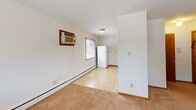 Located at 2384 Larpenteur Ave W in Lauderdale, Minnesota, this single-floor unit offers a practical and comfortable layout across several well-defined areas. The living space is finished with warm neutral carpet and features large windows fitted with horizontal blinds, allowing generous natural light and pleasant views of the surrounding greenery outside. A baseboard heating system runs along the perimeter walls, providing efficient climate control, while a wall-mounted air conditioning unit ensures year-round comfort. The kitchen is equipped with honey-toned wood cabinetry offering ample upper and lower storage, stone-patterned laminate countertops, a double stainless steel sink, and a white range. Light tile flooring extends through the kitchen area, which also accommodates a full-size refrigerator. The bedroom features the same plush carpeting as the living area and includes a sliding-door closet with a full-width hanging rod for organized storage. The bathroom is finished with floor-to-ceiling white ceramic tile surrounding a tub-shower combination, complemented by dark oil-rubbed bronze fixtures, a single vanity sink, and a well-lit mirror. Overall, the space presents a clean, functional environment with consistent finishes throughout.