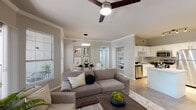 This single-floor residence offers a thoughtfully designed open-concept layout that seamlessly connects the living, dining, and kitchen areas. The living room is anchored by herringbone-patterned hardwood floors, crown molding, and a ceiling fan, with sliding glass doors that open to a private balcony and invite abundant natural light. The adjacent dining area features a large window with outdoor views and serves as an elegant setting for everyday meals. The kitchen is well-equipped with white shaker cabinets accented by gold hardware, a white quartz countertop island, stainless steel appliances, a herringbone tile backsplash, and a gold-toned faucet — combining both style and functionality. A set of built-in shelving near the hallway adds practical storage and display space. The bedroom is a serene retreat with plush carpeting, a ceiling fan, and a wide window that fills the room with natural light. A generously sized walk-in closet with wire shelving provides ample storage. The bathroom is finished with a white vanity, gold hardware accents, a bold black-framed mirror, and matching herringbone flooring, creating a clean and modern aesthetic throughout.