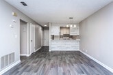 Located at 115 Mitchell Ave in LaGrange, Georgia, this single-floor home offers a well-organized layout with a cohesive, neutral color palette throughout. The open living and dining area is finished with wood-look plank flooring and features a stylish pendant chandelier, creating an inviting, functional space filled with natural light from a window with blinds. This area flows seamlessly toward the kitchen, which is defined by a peninsula counter clad in a light wood-tone finish, white cabinetry, a stainless steel sink, and pendant lighting above — offering both style and practicality. A textured ceiling adds dimension to the main living spaces. The hallway connects the living area to the private rooms and features additional storage closets. The bedrooms are carpeted for comfort, each with neutral walls, recessed or flush-mount ceiling lighting, and windows that bring in natural light and outdoor views. The bathroom is efficiently designed with wood-look tile flooring, a white vanity with cabinet storage, and a full tub-shower combination with built-in shelving. Clean white trim and consistent finishes throughout the home contribute to a cohesive and move-in-ready feel.