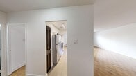 Located at 2220 Weston Rd in Toronto's Weston neighbourhood, this 2-bedroom, 1-bathroom unit offers a well-organized layout across a single floor. The living area is bright and open, featuring classic parquet wood flooring that runs throughout the unit and large windows that fill the space with natural light while framing views of the surrounding urban streetscape. Baseboard heaters are positioned beneath the windows, ensuring consistent warmth throughout the seasons.

The kitchen has been thoughtfully updated with crisp white cabinetry, grey quartz countertops, a stainless steel double-basin sink, and a striking herringbone marble-effect tile backsplash. Recessed lighting and tile flooring complete the clean, modern aesthetic. A hallway with a dark-panelled door connects the main living areas to the rest of the unit.

The spacious primary bedroom is notably generous in size, with parquet flooring, neutral white walls, and elegant dark double doors that add a sophisticated touch. The second bedroom is well-proportioned, featuring parquet flooring, a radiator, and a window with an urban outlook. The bathroom is finished with white subway tile surrounding a full bathtub and shower, complemented by a clean white vanity and mirror.