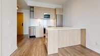 Located at 25 Nicholas in Toronto's vibrant Cabbagetown-St. James Town neighbourhood, this well-appointed one-bedroom, one-bathroom unit offers a thoughtfully designed layout with modern finishes throughout. Light hardwood-style flooring runs continuously across the living areas and bedroom, contributing to a cohesive and airy feel.

The open-concept kitchen is a standout feature, outfitted with light wood cabinetry, white quartz countertops, stainless steel appliances including a dishwasher, built-in microwave, and refrigerator. A peninsula with open shelving doubles as a breakfast bar and adds functional storage while defining the kitchen and living areas.

The bedroom is a quiet, bright retreat with a large window that invites natural light and offers outward views. Neutral wall tones and clean lines keep the space feeling fresh and uncluttered.

The bathroom is finished with large-format floor tiles, white subway-tiled walls, a soaking bathtub with an overhead rain showerhead, and a floating wood-toned vanity with a white countertop, completing the modern aesthetic. Track lighting in the main living area and flush-mount ceiling fixtures provide versatile illumination throughout. The unit's efficient design maximizes every square foot with a clean, contemporary sensibility.