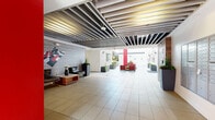 Located at 1558 Gordon St in the heart of Hollywood, Los Angeles, this modern residential building presents a thoughtfully designed lobby and common area experience. The main entry lobby immediately impresses with its striking industrial-style ceiling, composed of parallel metal slat beams that lend a bold architectural character to the space. Large-format light tile flooring extends throughout, creating a clean and cohesive aesthetic. A seating area near the entrance features leather lounge chairs arranged around a wood coffee table, complemented by a graphic chess-themed wall mural on a textured stone accent wall. A stainless steel elevator provides convenient vertical access, while a dedicated package locker system and a wall of individual mailboxes serve residents' everyday needs. The lobby opens seamlessly into a bright, open-air courtyard framed by white stucco walls and accented by a bold red structural column. The courtyard is furnished with vibrant red armchairs and side tables, creating a welcoming outdoor gathering space. Raised planters with lush greenery add natural elements throughout. A corridor lined with warm accent lighting connects to additional areas of the building. An on-site leasing office is accessible directly from the courtyard, rounding out a well-equipped and visually cohesive community space.
