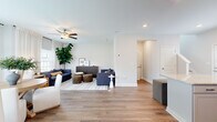 This two-story home offers a well-organized layout spread across two floors, combining functional design with modern finishes throughout. The main level features an open-concept kitchen and living area bathed in natural light from multiple windows dressed with sheer white curtains. The kitchen is outfitted with gray shaker-style cabinetry, granite countertops, a classic white subway tile backsplash, stainless steel appliances, and warm hardwood-style flooring that flows seamlessly into the living area. The living room is spacious and airy, complete with a ceiling fan and recessed lighting. A half bathroom is also conveniently located on the main floor. Upstairs, two bedrooms are connected by hallways and served by two additional full bathrooms. The generously sized primary bedroom features plush carpeting, large windows with natural light, and a dedicated walk-in closet with wire shelving. The secondary bedroom includes a double-door closet and soft carpeting, offering a comfortable and private retreat. The bathrooms feature clean, white finishes with tub-shower combinations. Two staircases provide easy access between floors, and additional hallway space enhances circulation throughout the home. The overall aesthetic is clean, bright, and contemporary.