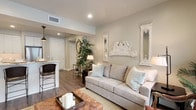 This thoughtfully designed single-floor residence blends modern convenience with a warm, cottage-inspired aesthetic. The living area serves as the heart of the home, showcasing neutral-toned walls, recessed lighting, and rich wood-look flooring that flows throughout the space. Shabby chic décor accents — including ornate white-framed mirrors and distressed wall pieces — add character, while large windows and a glass-panel door invite abundant natural light and provide access to an outdoor area. The kitchen is a standout feature, outfitted with crisp white shaker cabinetry reaching toward the ceiling, a classic subway tile backsplash, light stone countertops, a farmhouse-style sink, and a full suite of stainless steel appliances. A freestanding island adds additional workspace and storage. The residence includes two bedrooms, each offering a serene retreat with wood-look flooring, generous windows with blinds, and textured ceilings. The primary bathroom features a glass-enclosed walk-in shower with tile surround, a vanity with stone countertops, and direct access to a walk-in closet with built-in shelving. A second full bathroom provides a tub-shower combination with tiled walls and a marble-top vanity. The overall ambiance is calm, cohesive, and move-in ready.