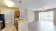 Located at 501 Hinson Dr in Myrtle Beach, SC, this single-floor unit offers a clean, open-concept design with a cohesive neutral color palette and light hardwood-style flooring extending throughout the space. The kitchen is a functional centerpiece, featuring warm wood cabinetry, granite-look countertops, a double-basin sink set into a peninsula that opens toward the living area, and black appliances including a refrigerator, range, and microwave. Generous upper and lower cabinet storage lines both sides of the galley-style kitchen corridor, providing ample organization space.

The open living area is bright and airy, benefiting from natural light streaming through large windows dressed with horizontal blinds. A ceiling fan overhead enhances comfort and air circulation. The layout flows seamlessly from the kitchen peninsula into the living space and toward a private entrance door, creating an accessible and practical arrangement.

Bedrooms continue the light flooring and neutral tones, each with ceiling fans and windows that bring in natural light. The bathroom includes a soaking tub and shower combination with a tiled surround, a wood-vanity with countertop, and hardwood-style flooring. A dedicated utility room accommodates washer and dryer hookups alongside a water heater, adding everyday convenience to the overall well-appointed layout.