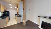 This unit at The Corner Lofts showcases an appealing blend of industrial heritage and contemporary design across a single floor. The space is anchored by striking exposed timber posts that serve as defining architectural elements, adding warmth and character throughout. Rich exposed brick walls complement the raw, loft-style aesthetic, while a ceiling fan and elevated ceiling height contribute to an open, airy atmosphere.

The living area features plush carpeting and flows naturally toward a balcony access door, allowing natural light to filter into the space. Louvered interior doors add a classic touch while maintaining practical functionality. The kitchen area transitions to light tile flooring and is equipped with light wood cabinetry, dark countertops, a sink, and pendant lighting overhead, providing a clean contrast to the industrial elements nearby. The open connection between the kitchen and living spaces enhances the overall sense of flow.

Throughout the unit, white walls keep the interior bright and neutral, allowing the exposed brick and timber posts to stand as focal points. The combination of original structural details and updated finishes gives this loft a distinctive character well-suited to urban living.