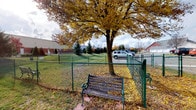 Located at 6049 Rings Ave in Grove City, Ohio, this single-floor property offers a notable outdoor environment that stands out for its natural character and functional layout. The exterior grounds feature a well-established mature tree providing generous shade and seasonal color, complemented by a neatly maintained green lawn. A chain-link fence encloses a dedicated outdoor seating area, which includes a classic bench with decorative iron armrests — an inviting spot for relaxation or informal gatherings. Evergreen shrubs and additional trees are planted throughout the grounds, contributing to a layered, landscaped appearance. Adjacent parking is accessible directly from the property, adding practical convenience. The surrounding neighborhood context includes neighboring structures and open green space, giving the property a community-oriented setting. The overall exterior ambiance is orderly and welcoming, with the natural landscaping elements providing a pleasant, park-like atmosphere. The single-story layout suggests ease of accessibility throughout the property. While interior imagery was limited, the exterior presentation reflects a property that is well-situated within its Grove City surroundings, suitable for a variety of uses.