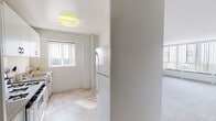 Located at 533 E 33rd Pl in Chicago's Bronzeville neighborhood, this single-floor unit offers a clean, functional layout filled with natural light. The spacious living area is carpeted and lined with large floor-to-ceiling windows dressed with vertical blinds, providing generous outdoor views and flooding the room with daylight. Baseboard heating runs along the window walls, ensuring comfort throughout the seasons. A pass-through opening connects the living area to the kitchen, enhancing the sense of openness between spaces. The kitchen features white cabinetry with ample upper storage, granite-style countertops, a gas range, a full-size refrigerator, and square tile flooring with a matching tile backsplash. A structural column adds a subtle architectural detail to the kitchen space. The bedroom is generously sized with plush carpeting, large windows offering outdoor views, and a built-in closet with double sliding doors providing practical storage. The bathroom is fully tiled in white, featuring a combined tub and shower, a pedestal-style vanity with under-cabinet storage, a mirrored medicine cabinet with integrated lighting, and a toilet. Throughout the unit, neutral tones and bright white walls create a clean, light, and welcoming atmosphere.