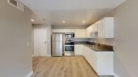 Located in Fontana, CA, this single-story home offers four bedrooms, one bathroom, and a thoughtfully arranged floor plan that maximizes every square foot. The kitchen is a standout feature, showcasing white shaker cabinetry, dark countertops, stainless steel appliances including a refrigerator, range, and built-in microwave, and a stainless steel sink. Light wood-style vinyl flooring runs throughout, lending a clean, cohesive look across the kitchen and adjacent living area. Recessed lighting and a textured ceiling add character to the main living space, which flows openly from the kitchen. The bedrooms are bright and functional, each featuring windows that allow natural light and views of outdoor greenery. The bathroom is appointed with white cabinetry, a dark countertop vanity, and a large mirror. Two closets provide additional storage, while a hallway connects the rooms efficiently. A patio extends the living space outdoors. Neutral warm-gray walls throughout create a calm, inviting atmosphere well-suited for comfortable everyday living.