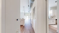 This thoughtfully designed single-floor space blends modern aesthetics with industrial-inspired details to create a bright and welcoming environment. The open-concept living area is anchored by wide-plank hardwood-style flooring that runs throughout, complemented by crisp white walls and abundant natural light streaming in through large floor-to-ceiling sliding glass doors. A ceiling fan and exposed metallic ductwork overhead lend an urban, loft-like character to the living space, while sheer curtain panels frame the outdoor view and soften the room's clean lines.

The galley-style kitchen is efficiently laid out and well-appointed, featuring white shaker cabinetry, classic subway tile backsplash, light countertops, and a full suite of stainless steel appliances including a refrigerator, range, microwave, and dishwasher. Pendant lighting above the kitchen pass-through adds warmth and connects the kitchen to the living area seamlessly.

A hallway leads to additional rooms, lined with louvered-door storage closets that offer generous organizational space. The bathroom features a full tub and shower combination with white subway tile surround, maintaining the clean, minimal aesthetic found throughout the unit. A smart thermostat near the entryway adds a contemporary, tech-forward convenience to the overall living experience.