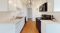 Located at 22555 Nadine Cir in Torrance, California, this single-floor residence offers a clean, functional layout designed for comfortable everyday living. The galley-style kitchen is well-appointed with white cabinetry, light countertops, a stainless steel sink, and black appliances including an electric range, built-in microwave, and dishwasher. Track lighting runs along the ceiling, providing focused illumination throughout the cooking space, which features warm hardwood-style flooring. Adjacent to the kitchen, the dining and living areas flow naturally together, with the same hardwood-style flooring extending through the common spaces. A ceiling fan with a light fixture serves the area, and a vertical-blind-covered sliding glass door allows natural light to fill the room. The living space transitions into carpeted bedroom areas, which are bright and neutral, each featuring windows with vertical blinds that bring in natural light. One bedroom includes mirrored sliding closet doors, maximizing both storage and the sense of space. The bathroom is finished with white cabinetry, a single vanity, wood-style flooring, and a tub-shower combination enclosed by frosted sliding glass doors. Throughout, the space maintains a bright, neutral palette with textured ceilings.