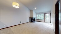 This single-floor residence offers a well-designed layout that balances comfort and functionality throughout its thoughtfully arranged spaces. The entryway features rich hardwood-style flooring that extends through the hallways and into the kitchen, providing a warm and cohesive transition between rooms.

The expansive living area is one of the home's standout features, boasting soaring vaulted ceilings that create an impressive sense of openness and volume. A corner brick fireplace serves as the focal point of the room, complemented by large windows and a glass door that invite abundant natural light and offer lush, tree-lined views of the surrounding landscape. Plush carpeting throughout the living area and bedrooms adds warmth underfoot.

The kitchen is equipped with dark espresso cabinetry, granite countertops, and stainless steel appliances including an electric range and over-the-range microwave. A pass-through counter connects the kitchen to the living space, enhancing the open-concept flow.

The bedrooms are generously proportioned and carpeted, each featuring large windows with views of the greenery outside and baseboard heating for year-round comfort. The bathrooms are finished with extended vanity countertops, dark cabinetry, and mirrored medicine cabinets, delivering a clean and practical aesthetic throughout this well-appointed residence.