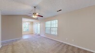 This single-floor residence offers a practical and comfortable layout across several well-defined living areas. The main living room is a notably spacious area finished with neutral-toned carpet and features vaulted ceilings that enhance the sense of openness. A ceiling fan with a light kit provides both airflow and ambient lighting, while multiple windows dressed with vertical blinds allow generous natural light to fill the space. The adjoining dining area is accessible through an open passage and is illuminated by a classic chandelier, adding a touch of warmth.

The galley-style kitchen is efficiently organized, featuring light wood cabinetry, dark granite-look countertops, and light hardwood-style flooring. Black appliances — including a refrigerator, electric range, and over-the-range microwave — are neatly integrated into the layout. A window near the dining area brings in additional natural light.

The bedrooms are carpeted and finished in neutral tones, each equipped with a ceiling fan and windows that provide natural light and ventilation. The primary bedroom benefits from vaulted ceilings, adding visual spaciousness.

The bathroom includes a single-sink vanity with wood cabinetry, a large mirror, and a full tub-shower combination with clean white surrounds, complemented by light hardwood-style flooring.