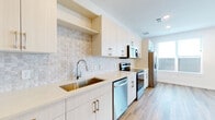 This single-floor space showcases a clean, contemporary design carried consistently throughout. The kitchen is a standout feature, outfitted with light wood-toned cabinetry, brushed gold hardware, and quartz countertops. A textured mosaic tile backsplash adds visual depth, while stainless steel appliances — including a dishwasher, electric range, over-the-range microwave, and refrigerator — provide full functionality. An undermount sink with a pull-down faucet completes the well-appointed layout.

Light wood-toned luxury vinyl plank flooring runs throughout the living areas and bedrooms, lending warmth and continuity to the space. The bedrooms are bright and open, benefiting from natural light through sizable windows with blinds, recessed lighting, and ceiling fans. At least one bedroom includes access to a walk-in closet with built-in shelving for organized storage.

The bathroom features a tub-shower combination with striking marble-style surround tile, white cabinetry with gold hardware, quartz countertops, and wood-look flooring. The overall palette of whites, warm neutrals, and natural wood tones creates a cohesive, fresh aesthetic throughout the entire unit.