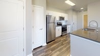 Located at 10001 E Dry Creek Rd in Englewood, Colorado, this single-floor residence offers a well-designed, contemporary living space with a cohesive aesthetic throughout. The open-concept layout connects the living and dining areas to a modern kitchen, which is outfitted with stainless steel appliances — including a refrigerator, range, and microwave — white cabinetry, dark countertops, and a peninsula that provides both additional workspace and a natural dividing point between the kitchen and living area. Rich, wood-look plank flooring runs through the main living spaces, adding warmth and visual continuity. A pendant light fixture over the dining area adds a stylish focal point, while large windows fitted with horizontal blinds allow ample natural light to fill the space.

The bedroom features plush carpeting underfoot, a ceiling fan with integrated lighting, and a window offering outdoor views of the surrounding Englewood landscape. A second carpeted room is also present, equally bright with its own window. The bathroom is finished with the same wood-look flooring as the main areas and includes a dark-countertop vanity with white cabinetry, an undermount sink, and a clean, neutral color palette. Throughout the unit, gray-toned walls and white trim create a modern, move-in-ready environment.