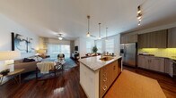 This single-floor residence offers a thoughtfully designed open-concept layout that seamlessly connects the kitchen, dining, and living areas. The kitchen is a standout feature, equipped with stainless steel appliances including a French door refrigerator, electric range, and over-the-range microwave. A large central island with granite countertops and an undermount sink serves as the focal point, complemented by modern wood-tone cabinetry, subway tile backsplash, and pendant lighting overhead. Rich hardwood flooring flows throughout the main living areas, adding warmth and continuity to the space. The living room is bright and welcoming, with a ceiling fan, floor-to-ceiling sliding glass doors that invite natural light, and access to an outdoor area. The dining space adjacent to the kitchen benefits from large windows that further enhance the airy atmosphere. The bedroom is generously sized, featuring plush carpeting, multiple windows with blinds and curtain accents, and a ceiling fan. The bathroom is well-appointed with a full soaking tub, tile surround, granite vanity, and modern cabinetry, with hardwood flooring extending into the hallway. Throughout the residence, clean white walls and consistent finishes create a cohesive, contemporary aesthetic.