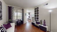 This well-appointed single-floor residence offers a thoughtfully designed layout that balances style and functionality throughout. The living area is anchored by warm wood-style flooring and features a striking accent wall adorned with a grid of black square frames, adding a bold graphic element to the neutral palette. Large sliding glass doors flood the space with natural light and provide views of lush outdoor greenery, while vertical blinds and decorative curtains offer privacy. The open flow connects seamlessly to a bright dining area, which benefits from its own large window and a modern pendant light overhead, with wall-mounted shelving providing a decorative focal point. The kitchen is efficiently laid out with white cabinetry, granite-style countertops, a breakfast bar, and full appliances including a refrigerator and range. The bedroom is a calm retreat, featuring plush carpeting, a large window with layered curtains, and ample closet space. Two full bathrooms each include a soaking tub and shower combination, granite-style vanity countertops, white cabinetry, and rich wood-style flooring that ties the space together cohesively. Throughout, the residence maintains a clean, contemporary aesthetic with warm tones and inviting finishes.