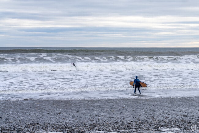 A person with a surfboard walks into the oncoming waves in Hampton.
