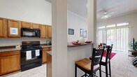 This thoughtfully designed single-floor unit offers a cohesive layout that maximizes comfort and functionality. The living area is an immediate standout, boasting dramatically tall ceilings with crown molding, plush carpeting, and a ceiling fan. Floor-to-ceiling sliding glass doors flood the space with natural light and provide access to an outdoor area, while transom windows above amplify the airy, open atmosphere.

The kitchen is well-appointed with warm honey-toned wood cabinetry, dark granite-style countertops, tile flooring, and a full suite of appliances including a stainless steel refrigerator, black electric range, and built-in microwave. A peninsula with a breakfast bar seamlessly connects the kitchen to the dining and living areas, making it ideal for casual dining and entertaining.

The bedrooms are carpeted and feature impressively tall ceilings that enhance the sense of space. The primary bedroom includes direct access to a private bathroom, while ample closet space is provided throughout. Neutral wall tones carry through the entire unit, creating a clean and versatile backdrop. Overall, the space offers a bright, open ambiance with a practical and well-considered design.