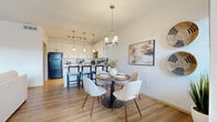 This thoughtfully designed single-floor residence offers a cohesive blend of modern aesthetics and practical functionality. The open-concept kitchen is outfitted with crisp white cabinetry, granite countertops, a full suite of black appliances including a top-freezer refrigerator and electric range, and light wood-look flooring that extends throughout the main living areas. A breakfast bar with barstool seating connects the kitchen seamlessly to the dining space, which is anchored by a stylish pendant chandelier and benefits from natural light through large windows. The living room is bright and welcoming, featuring a ceiling fan, access to an outdoor area via a glass door, and views of the surrounding exterior. The primary bedroom is generously sized with plush carpeting, direct access to an outdoor space, and additional windows that bring in natural light. A secondary bedroom, also carpeted and ceiling fan-equipped, offers comfortable accommodations. The primary bathroom features a walk-in glass-enclosed shower, granite-topped white vanity, and wood-look flooring. A dedicated in-unit laundry room provides full-size side-by-side washer and dryer units with built-in shelving above. Clean white walls and consistent finishes throughout create a bright, cohesive living environment.