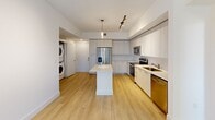 This well-appointed 2-bedroom, 3-bathroom single-floor residence offers a thoughtfully designed layout with a clean, contemporary aesthetic. The open-concept kitchen is a standout feature, showcasing flat-front cabinetry in a light wood finish, stainless steel appliances including a French door refrigerator, range, microwave, and dishwasher, and a central island with a crisp white quartz countertop. Track lighting and pendant fixtures illuminate the space, while light hardwood-style flooring extends throughout the unit, creating a seamless, cohesive look. A stacked in-unit washer and dryer adds everyday convenience. The two bedrooms are bright and airy, with white walls, light flooring, and windows fitted with horizontal blinds that offer views of lush greenery. The primary bedroom connects directly to its en-suite bathroom, which features a large walk-in glass-enclosed shower with floor-to-ceiling beige tile, mosaic tile flooring, and polished chrome fixtures. A separate vanity area includes a white quartz countertop and a wide mirror. The additional bathrooms maintain the same clean, modern finishes. Three closets provide ample storage throughout. The overall ambiance is bright, minimalist, and move-in ready.