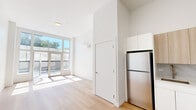 Located at 1 Lyon Pl, Unit 1D in White Plains, NY, this thoughtfully designed studio offers a clean, modern aesthetic across a single floor. The open-concept layout maximizes the use of space, seamlessly connecting the kitchen and living area under soaring ceilings that enhance the sense of openness.

The kitchen is a standout feature, equipped with stainless steel appliances including a full-size refrigerator, electric range, and over-the-range microwave. Cabinetry combines crisp white lower units with warm wood-tone upper cabinets, complemented by a marble-style backsplash and light countertops, creating a refined and functional workspace.

The living area is bathed in natural light from floor-to-ceiling windows and a glass sliding door that opens to an outdoor area, flooding the space with sunlight and providing views of greenery. Light-toned hardwood flooring runs throughout, reinforcing the bright, airy atmosphere. A wall-mounted split HVAC unit ensures year-round comfort.

The bathroom is finished with modern, neutral materials, featuring a wood-vanity with an integrated sink, a sleek mirror, a contemporary toilet, and a striking marble-style accent wall, all set on light, seamless flooring. Clean white walls and recessed lighting complete the polished look of this well-appointed unit.