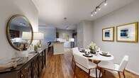 Harbor Cove presents a thoughtfully designed 1-bedroom, 1-bathroom residence that maximizes every square foot through an efficient, open-concept floor plan. Rich hardwood-style flooring flows throughout the main living areas, creating a warm and cohesive aesthetic. The living room is a standout space, featuring a tray ceiling, a ceiling fan, and large French doors with transom windows that invite abundant natural light and views of the outdoors. The dining area sits adjacent to the kitchen and is illuminated by modern track lighting, offering a seamless transition between spaces. The kitchen features a breakfast bar with counter seating, stainless steel appliances including a refrigerator and range, and ample cabinetry with warm wood tones. The bedroom is a comfortable retreat, complete with plush carpeting, a ceiling fan, a large window, and access to a walk-in closet outfitted with wire shelving and hanging rods. The bathroom is appointed with rich wood cabinetry, granite countertops, and hardwood-style flooring. A dedicated in-unit laundry room with full-size washer and dryer hookups and built-in shelving adds significant everyday convenience. The overall ambiance is modern, clean, and inviting throughout.