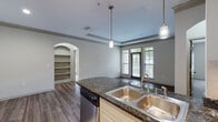 Located at 1460 Distribution Dr in Suwanee, GA, this single-floor residence offers a well-designed layout with a blend of modern finishes and functional living spaces. The open-concept kitchen serves as a central highlight, featuring granite countertops, a large double-basin sink, stainless steel appliances including a refrigerator, range, microwave, and dishwasher, along with white cabinetry and pendant lighting. A kitchen island provides additional prep space and flows seamlessly into the main living area. Tray ceilings with crown molding add architectural character throughout, while rich hardwood-style flooring extends across the main living spaces. The living area benefits from large windows and a glass door that opens to an outdoor balcony, filling the room with natural light and views of the surrounding greenery. Bedrooms are carpeted for comfort, each equipped with ceiling fans and windows that invite natural light. The bathrooms feature granite vanity tops, tile flooring, and full tub-shower combinations. A dedicated laundry room accommodates a full-size washer and dryer. Additional details include a built-in electrical panel, an arched entryway with built-in shelving, and track lighting in the kitchen area, contributing to an overall polished and functional living environment.