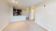 This single-floor unit offers a thoughtfully designed open-concept layout that seamlessly connects the kitchen, dining, and living areas. The kitchen is a standout feature, showcasing rich dark-toned cabinetry with sleek hardware, granite-look countertops, a tile backsplash, and a full suite of stainless steel appliances including a range, microwave, and refrigerator. Warm hardwood-style flooring grounds the kitchen space, which flows into a peninsula with pendant lighting overhead — ideal for casual dining or entertaining.

The living area transitions naturally from the kitchen, featuring soft wall-to-wall carpeting and neutral beige tones that create a calm, inviting atmosphere. A set of French doors opens to a private balcony, allowing natural light to fill the space and offering views of the surrounding area. A secondary windowed room with carpeting provides additional flexible living space.

The bathroom is well-finished with large-format tile flooring, a dark wood vanity with granite-style countertop, a full soaking tub with subway tile surround, and a combination shower fixture. Throughout the unit, clean white trim, neutral walls, and consistent modern finishes create a cohesive and polished aesthetic.