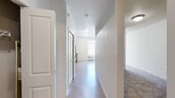 Located at 22401 E Clairmont Ln in Liberty Lake, Washington, this single-floor unit offers a well-organized layout designed to maximize its modest footprint. The space is finished with a clean, neutral palette of white and warm beige tones, creating a bright and cohesive atmosphere throughout.

The kitchen serves as a functional centerpiece, featuring warm wood-tone cabinetry, a full suite of black appliances including a refrigerator, electric range, built-in microwave, and dishwasher, along with light countertops and a single-basin sink. Track lighting overhead enhances visibility, while a large window invites natural light and provides views of the surrounding greenery.

A central hallway connects the main living areas, finished with light hardwood-style flooring that flows seamlessly through the open spaces. The living and sleeping areas offer a mix of hardwood-style and carpeted flooring, providing comfort and practicality. The textured ceilings and clean white walls contribute to a tidy, move-in-ready aesthetic.

The bathroom is efficiently appointed with a sliding glass walk-in shower, a vanity with a single sink and mirror, wood-toned cabinetry, and hardwood-style flooring, maintaining the consistent design language of the unit. Overall, the space presents a practical and comfortable environment suited for everyday living.