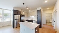Located at 2101 Bond Street in Charlottesville, Virginia, this thoughtfully designed two-bedroom, one-bathroom residence offers a clean, modern aesthetic across its single floor. Light hardwood flooring flows consistently throughout the space, creating a warm and cohesive feel.

The open-concept kitchen and living area serves as the heart of the home. The kitchen is a standout feature, showcasing a two-tone cabinet design with dark lower cabinets and cream upper cabinets, a white subway tile backsplash, and striking quartz countertops with elegant veining. A central island provides additional prep space and casual seating potential. Stainless steel appliances, including a refrigerator, range, microwave, and dishwasher, complete the well-appointed kitchen. Sleek pendant lighting adds a modern touch overhead.

The living area is bright and open, with recessed lighting and a neutral white palette that maximizes the sense of space. Both bedrooms feature the same light hardwood floors and clean white walls, with the second bedroom benefiting from a window that brings in natural light and outdoor views. A dedicated walk-in closet with wire shelving provides generous storage.

The bathroom is finished with neutral large-format tile, a gray vanity with modern hardware, and a soaking tub, delivering a clean and functional design.