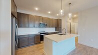 This well-designed single-floor residence offers a cohesive blend of modern finishes and functional layout throughout. The heart of the home is an open-concept kitchen, showcasing rich dark-brown cabinetry that extends to the ceiling for ample storage, complemented by white quartz countertops, a classic subway tile backsplash, and stainless steel appliances including a range and built-in microwave. A generously sized central island with an integrated sink serves as both a prep area and a gathering point, illuminated by a pair of stylish glass pendant lights. Wood-look flooring runs throughout the main living and kitchen areas, lending warmth and continuity to the space. The bedrooms are finished with plush carpeting and ceiling fans, with windows that invite natural light and outdoor views. A spacious walk-in closet offers wire shelving on multiple walls for organized storage. The bathrooms maintain a consistent design aesthetic, featuring dark wood vanities with white countertops and wood-look flooring. One bathroom includes a glass-enclosed walk-in shower, while another offers a full soaking tub and shower combination. The overall ambiance is clean, contemporary, and move-in ready, with neutral tones creating a versatile backdrop throughout.
