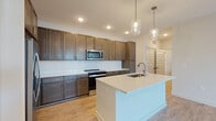 This well-designed single-floor residence offers a cohesive blend of modern finishes and functional layout throughout. The heart of the home is an open-concept kitchen, showcasing rich dark-brown cabinetry that extends to the ceiling for ample storage, complemented by white quartz countertops, a classic subway tile backsplash, and stainless steel appliances including a range and built-in microwave. A generously sized central island with an integrated sink serves as both a prep area and a gathering point, illuminated by a pair of stylish glass pendant lights. Wood-look flooring runs throughout the main living and kitchen areas, lending warmth and continuity to the space. The bedrooms are finished with plush carpeting and ceiling fans, with windows that invite natural light and outdoor views. A spacious walk-in closet offers wire shelving on multiple walls for organized storage. The bathrooms maintain a consistent design aesthetic, featuring dark wood vanities with white countertops and wood-look flooring. One bathroom includes a glass-enclosed walk-in shower, while another offers a full soaking tub and shower combination. The overall ambiance is clean, contemporary, and move-in ready, with neutral tones creating a versatile backdrop throughout.