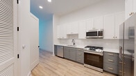 Located on Boulevard SE in Atlanta's historic Grant Park neighborhood, this single-floor unit showcases a clean, contemporary design with light hardwood-style flooring running throughout. The kitchen is a standout feature, equipped with two-tone cabinetry—crisp white upper shaker-style cabinets paired with gray lower cabinets accented by gold hardware. Stainless steel appliances include a gas range, built-in microwave, dishwasher, and a French door refrigerator, all complemented by white quartz countertops and a classic subway tile backsplash. A matte black faucet over a single-basin sink adds a modern contrast.

The living and bedroom areas are bright and open, with neutral white walls and natural light filtering through windows with views of the surrounding greenery. A ceiling fan is present in one of the main living spaces, contributing to the airy atmosphere.

A dedicated laundry area houses a stacked Samsung washer and dryer unit alongside built-in shelving, offering practical in-unit convenience. The bathroom features a full soaking tub with white subway tile surround, gray vanity cabinetry, and matte black fixtures that tie cohesively into the overall design. The consistent use of light tones and modern finishes throughout creates a cohesive and functional living environment.